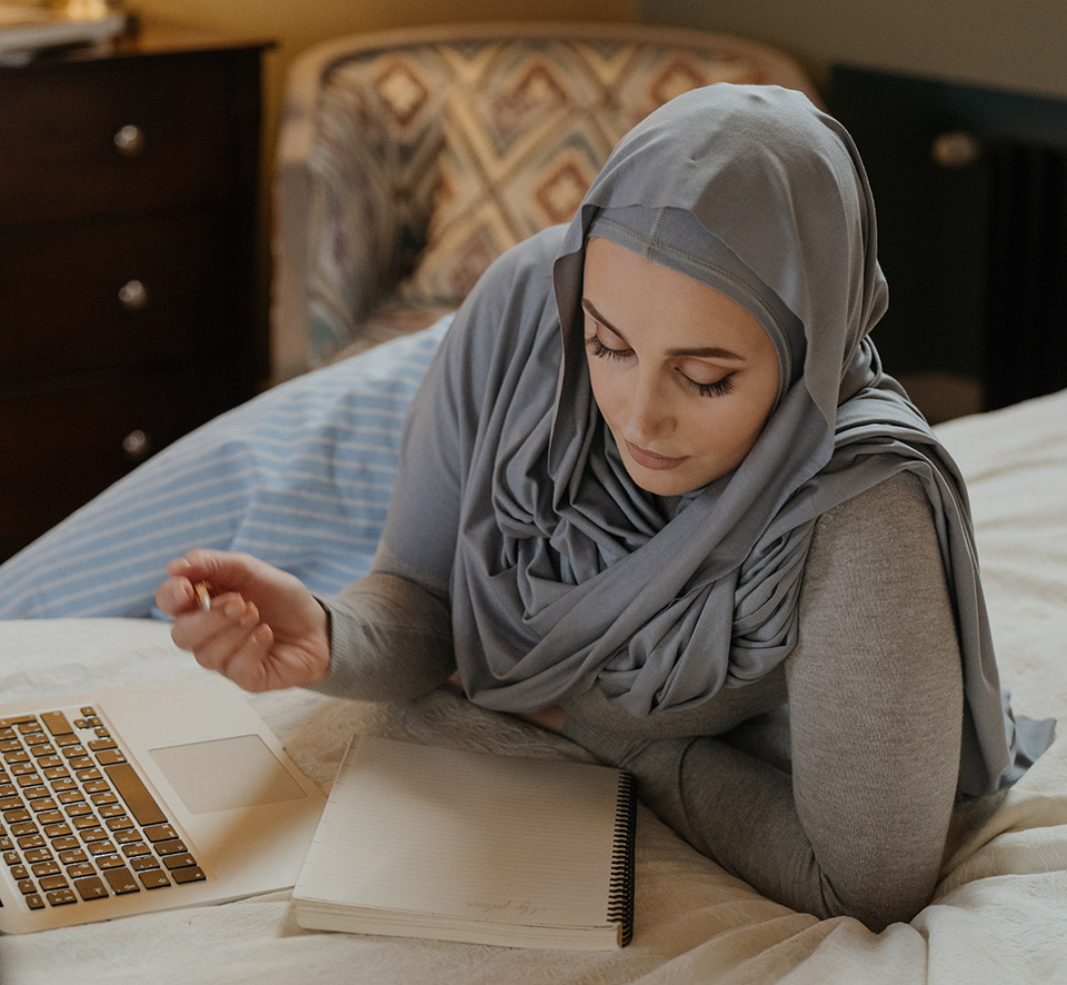 Kvinna i hijab halvligger framför en dator.